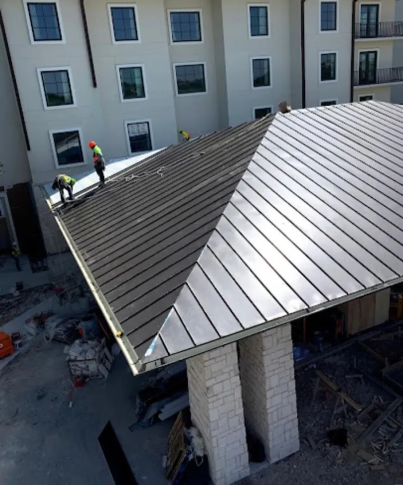Crew installing standing seam metal roof panels on a commercial project in Huntley